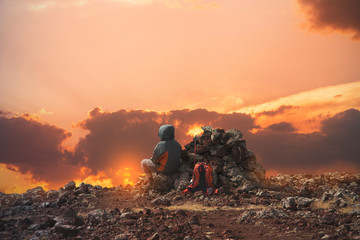 A female hiker sits on top of a mountain after climbing a mountain and looks at  beautiful sunset.	