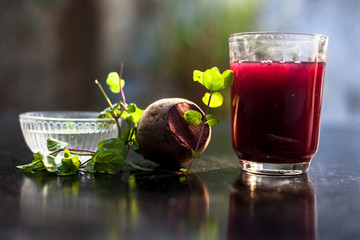 Beetroot smoothie in a glass on black glossy surface with some fresh mint leaves and...