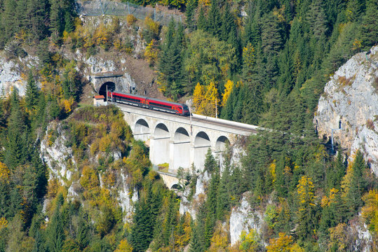 Red train on a viaduct between two tunnels on the Semmering Railway. The Semmering Railway is the oldest mountain railway of Europe and a Unesco World Heritage site.