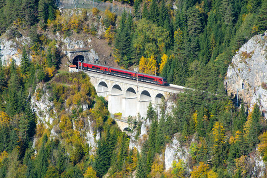 Red train on a viaduct between two tunnels on the Semmering Railway. The Semmering Railway is the oldest mountain railway of Europe and a Unesco World Heritage site.