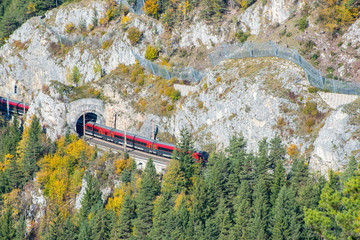 Red train on a viaduct between two tunnels on the Semmering Railway. The Semmering Railway is the...