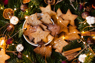 Homemade cookies with the french text Happy Holidays! Handmade freshly backed gingerbread biscuits served in a white bowl and decorated with christmas lights, fir, citrus, cotton, anise and cinnamon