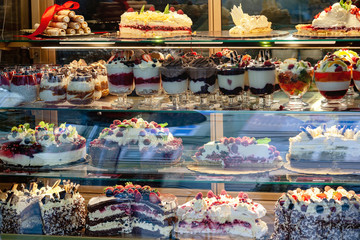 A variety of desserts and cakes in the window of a pastry shop in Krakow. Reflection of the buildings opposite in the shop window