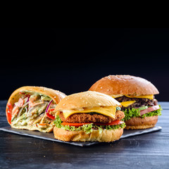 Burgers with juicy cutlet, fresh vegetables, crispy bun with sesame seeds on a wooden table. Traditional fast food.