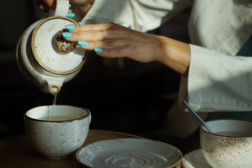 Girl with manicure pours herself green tea from a teapot in a restaurant