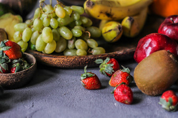Photo of fresh strawberries with the strawberry leaf on rustic grey background. A bunch of ripe strawberries on the table with lemon grape kiwi banana. Copy space. Organic food. Clear food.