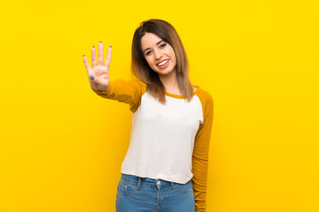 Pretty young woman over isolated yellow wall happy and counting four with fingers