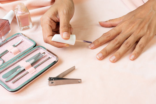 Female hands doing nail polish in pearl pink color with set of manicure instruments and tools  on pink silk velvet. beauty, manicure concept