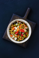 Olive salad for muffuletta in a bowl on a dark wooden board.