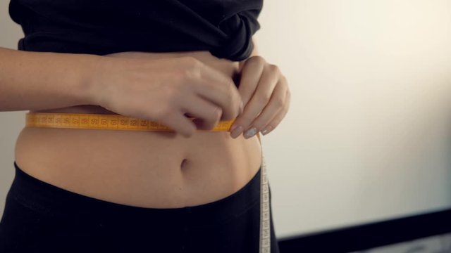 Closeup of a woman's waistline with a tape measure around her flat