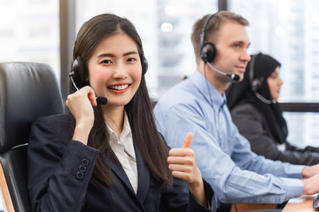 Happy smiling operator asian woman is customer service agent with headsets working on computer in a call center, talking with customer for assisting to resolve the problem with her service mind