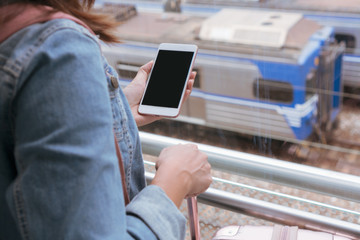 Young traveller girl in jeans jacket with smart phone, pink bag and luggage waiting for the train on the platform, copy space, travel or transportation concept