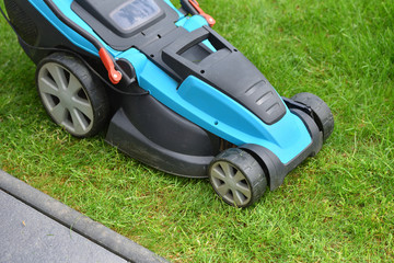 An electric lawn mower cuts the lawn near the edge and concrete curb. Close-up