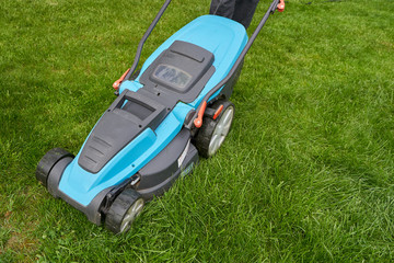 Electric lawn mower mows a bright green overgrown lawn, close-up