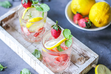 Photo of refreshing summer Strawberry infused waters. Mineral water with fresh strawberries lemon mint with a grey background. Detox water with strawberry lemon mint. Copy space. Wooden box