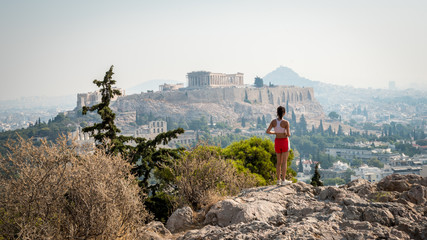 Teen in red shorts standing on hill with Parthenon in the background