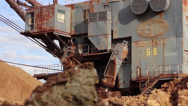 A huge, old dragline turns, doing its job. Mining excavator close-up on a background of heaps of sand.