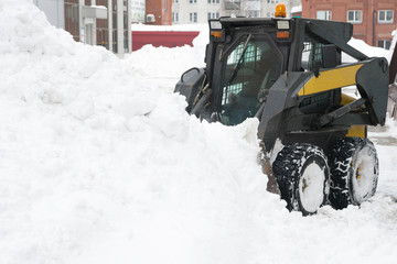 Snow drift. Snow plow compact tractor rakes a large snowdrift. Copy space.