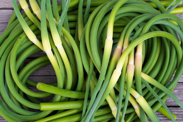 Green stalks of garlic on wooden table. The twisted stems of plants from seed. Preparation of summer salad for healthy diet