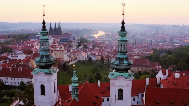 Aerial view over Strahov monastery at sunrise. Lateral shot, drone circling above belfries of cathedral in twilight at time before sun rising, showing picturesque panorama above Prague in morning