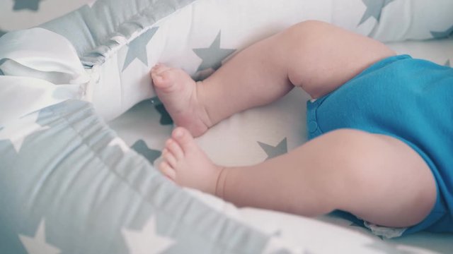 adorable newborn child in azure clothes bothers funny little leg in conformable cocoon extreme close view