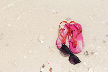 Black sunglasses and pink shoes on the sea beach on the Summer.