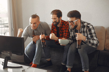 Fans sitting on the couch in the living room. Guys drinking a beer