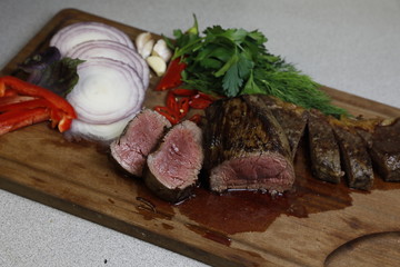 Beef steaks grilled and captured on a cutting wooden board with vegetables, organic red onion, paprika, pepper, green: dill and parsley, red chili pepper and garlic. Top view.