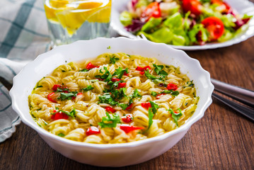 instant noodles in white bowl on wooden table background and vegetables salad on plate