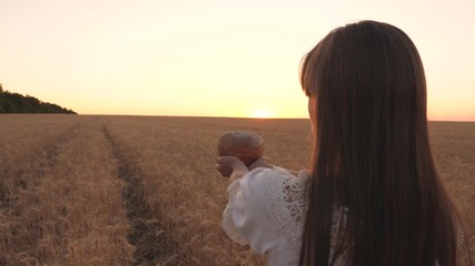 delicious bread on the palms of a young woman. loaf of bread in hands of girl over wheat field in rays of sunset. close-up.Delicious bread in hands carries young beautiful woman on wheat field.