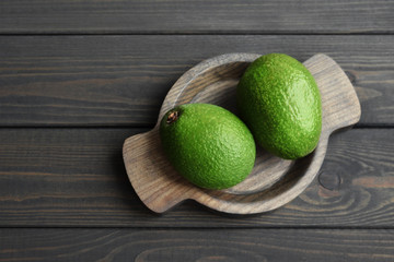 Fresh organic avocado in wooden plate over dark wooden table background