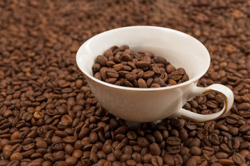 a cup with coffee grains is immersed in a scattering of other beans
