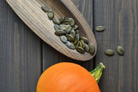 Fresh raw orange pumpkin with dry green pumpkin seeds on wooden plate over dark old wooden table background, top view.