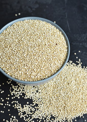 Bowl of healthy white uncooked quinoa seeds on dark stony background