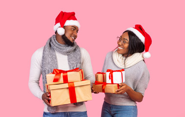 Festive afro couple holding xmas gifts, looking at each other