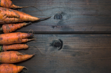 Ugly carrots on the left on wooden background freshly picked from garden. Organic food concept.