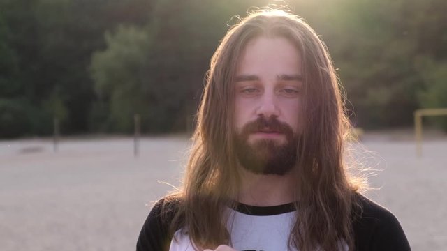 Close up, Portrait of a handsome Caucasian bearded young man with long hair looking artistic at camera in the sunset.