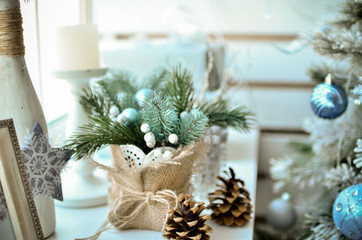 Christmas decor in bright colors stands near the window. Fir branches in a wooden vase. A light photo in pastel colors was taken on a bright day.