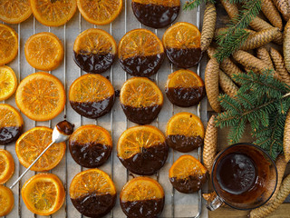 Christmas sweets, candied fruits in chocolate. Caramelized orange slices on a light paper background. Homemade dessert. Slices laid out on paper, top view. Decor - branches and cones of spruce.