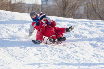 Two boys riding together at the sledge on snowy hill