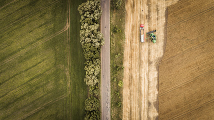 Aerial view of a combine unloads grain from grain compartment into a truck. One truck drove off and the next truck drove up to receive wheat grains.