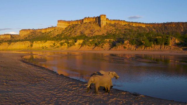 Spectacular aerial zoom out view of sunlight shining on the beautiful red sandstone Chilojo cliffs with elephants drinking in the Runde river below, Gonarezhou National Park, Zimbabwe