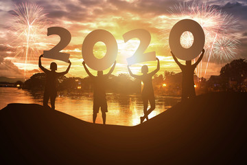Silhouette young people hold on New year 2020 logo with sky background at sunset