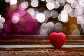 Red heart ball on wood table with light bokeh background.