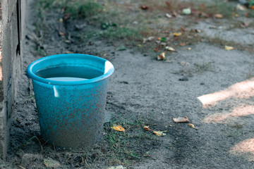 Blue plastic bucket full of water in the garden. Dirty garden tools © Klochkov