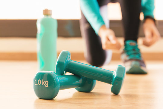 Stock photo of two dumbbells and a bottle. In the background a young woman preparing to train
