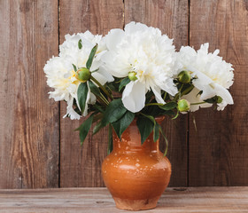 Bouquet of white peonies in a clay jug on rustic wooden background