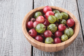 Fresh green and red gooseberries in a bamboo bowl on a wooden table. Top view