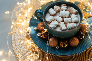 Cup of hot chocolate with marshmallows decorated Christmas baubles and defocused lights on gray wooden background. Christmas and New Year holidays