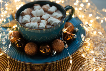 Cup of hot chocolate with marshmallows decorated Christmas baubles and defocused lights on gray wooden background. Christmas and New Year holidays
